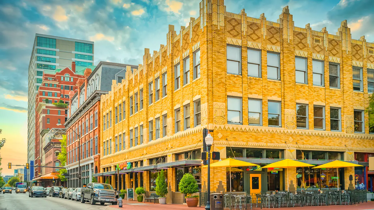 A historic yellow brick building on a city street corner, featuring a restaurant with an outdoor patio and bright yellow umbrellas.