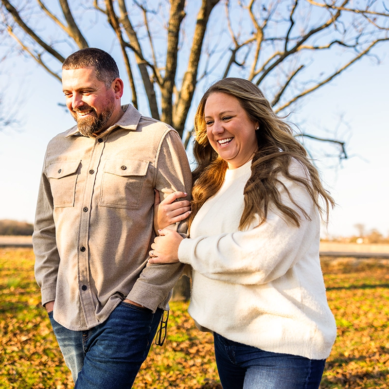 A happy couple walking outdoors in a field, with the woman linking her arm through the man's.