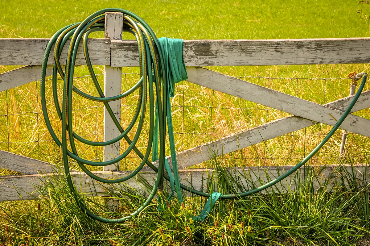 Green hose on a fence in a field.